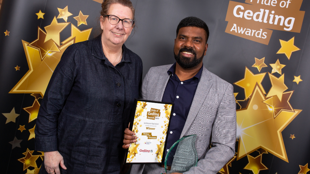 Business in the Community Award Winner Suthaharan Raslinghan (right) with a representative from Keepmoat Homes (left) stood in front of a black Pride of Gedling Awards banner with gold stars and text on it.