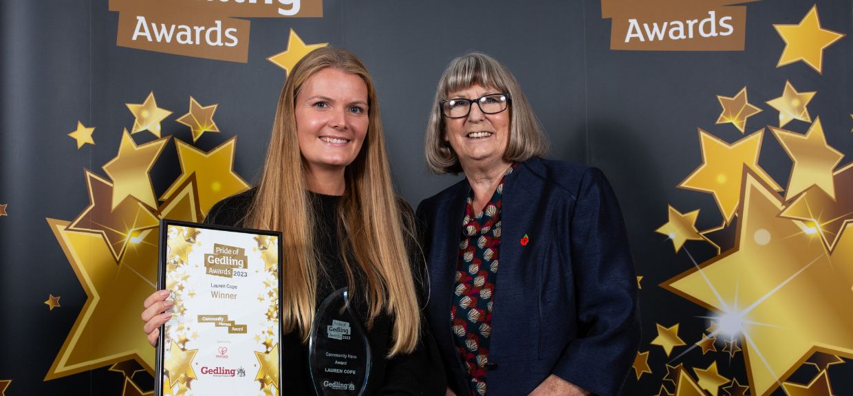 Community Hero Award Winner Lauren Cope, stood against the Pride of Gedling black and gold backdrop next to a representative from the category Sponsors